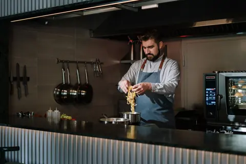 Kock som lägger upp pasta i det öppna köket.
