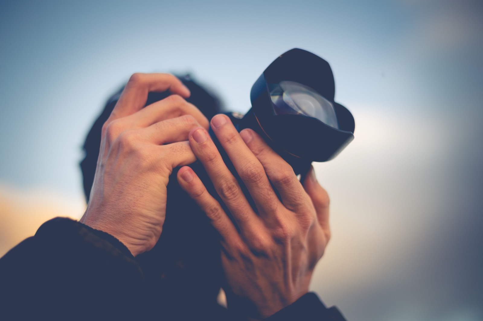 Fotograf som håller en kamera med zoomlins mot en klarblå himmel